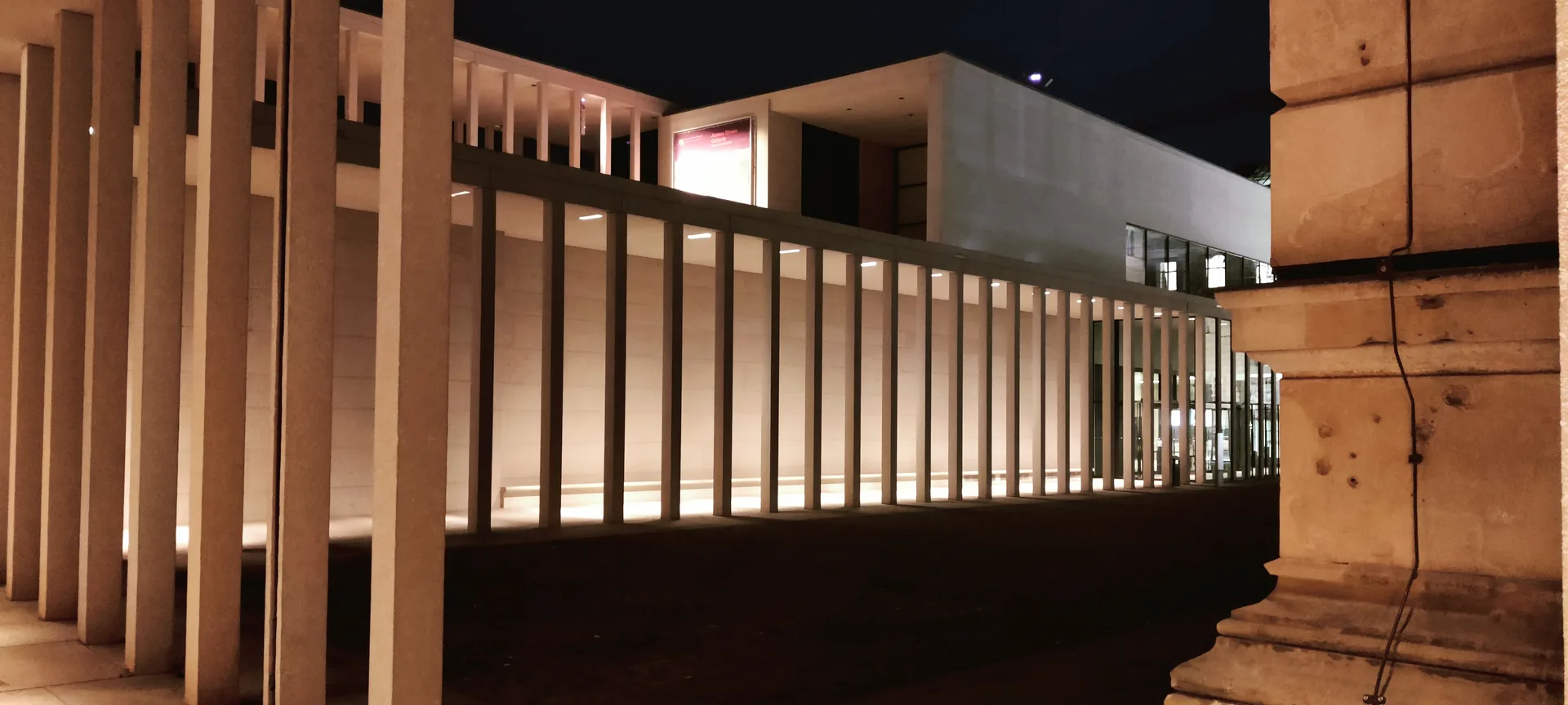 Photo d'une colonnade moderne aux piliers droits et éclairés dans la nuit, la pierre ancienne d'un autre bâtiment au premier plan