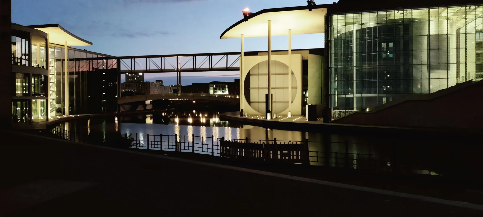 Photo des bâtiments du quartier gouvernemental au bord de la Spree, la passerelle et les lumières se reflétant dans l'eau