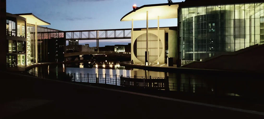 Photo des bâtiments du quartier gouvernemental au bord de la Spree, la passerelle et les lumières se reflétant dans l'eau