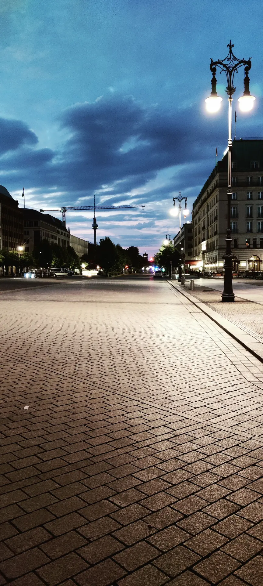 Photo d'une large avenue pavée et vide, un lampadaire à droite, la tour de télévision et une grue à l'horizon