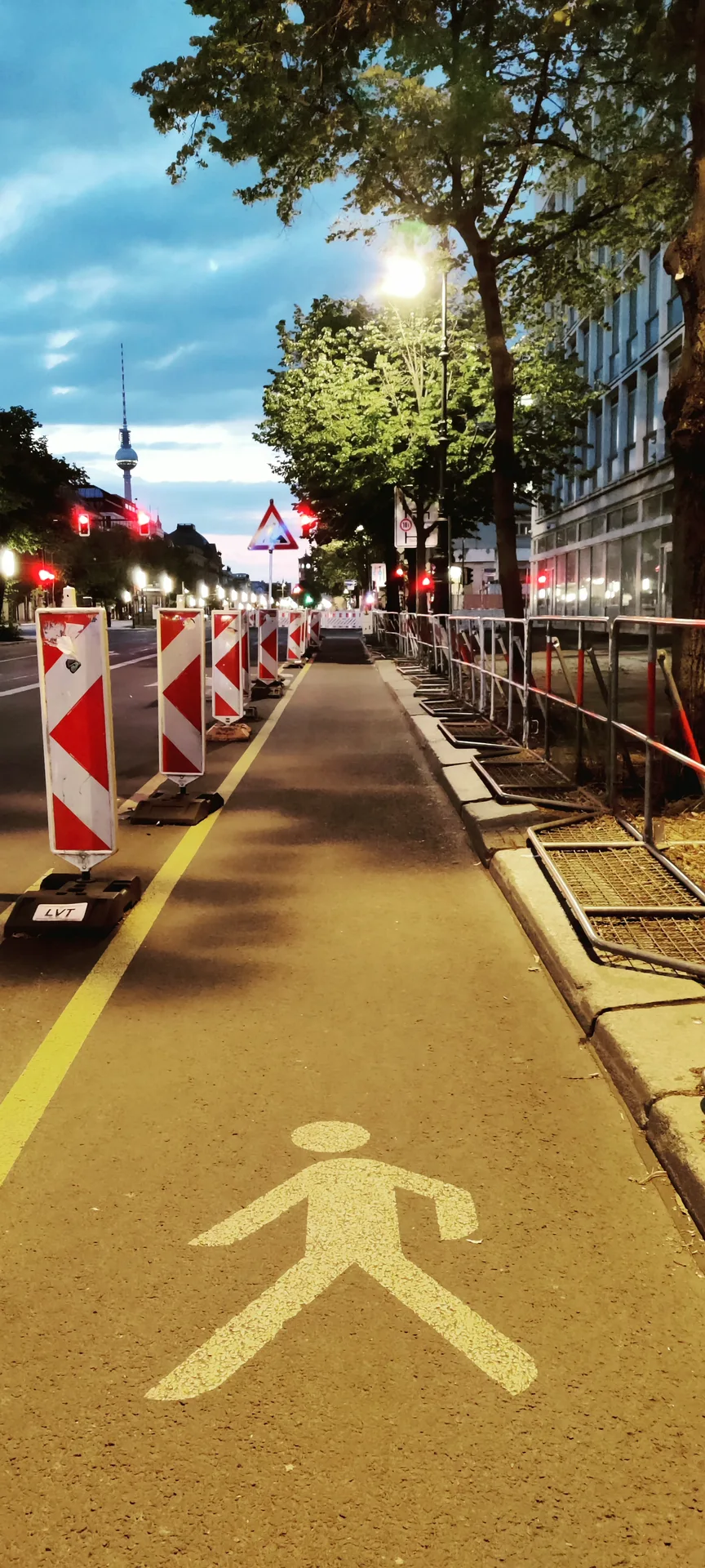 Photo d'un cheminement piéton balisé de barrières de chantier, un marcheur peint au sol, le tout baigné dans la chaude lumière des lampadaires